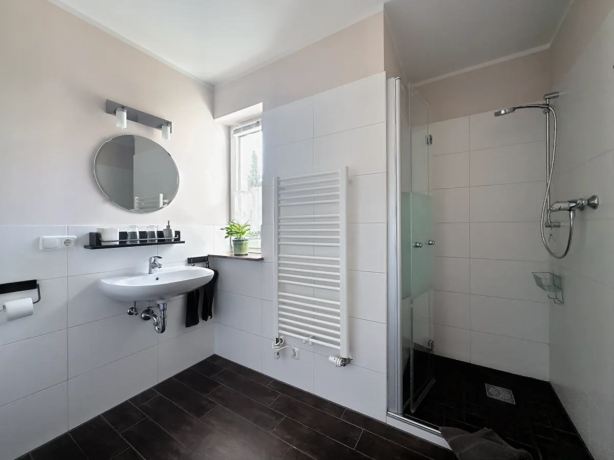 Modernes Badezimmer der Ferienwohnung 2 mit begehbarer Dusche, weißem Waschbecken und Handtuchheizkörper