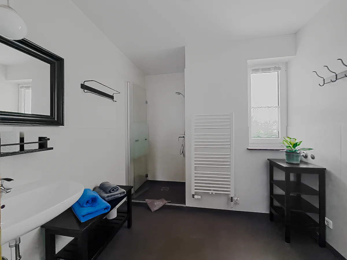 Modernes Bad der Ferienwohnung 3 mit ebenerdiger Dusche, weißem Handtuchheizkörper und Fenster.