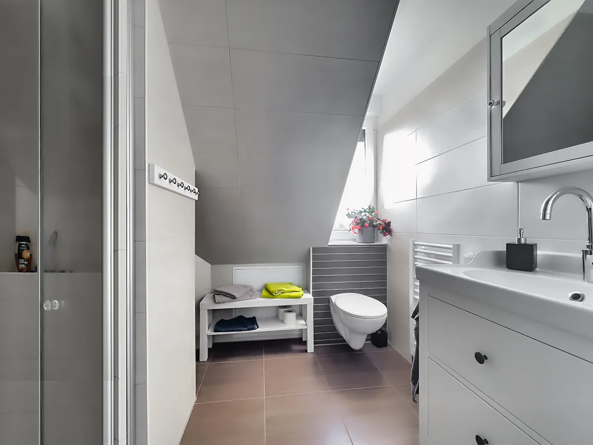 Helles Tageslichtbad in Ferienwohnung 5 mit modernem WC, weißem Waschtisch und Handtuchheizkörper unter der Schräge.
