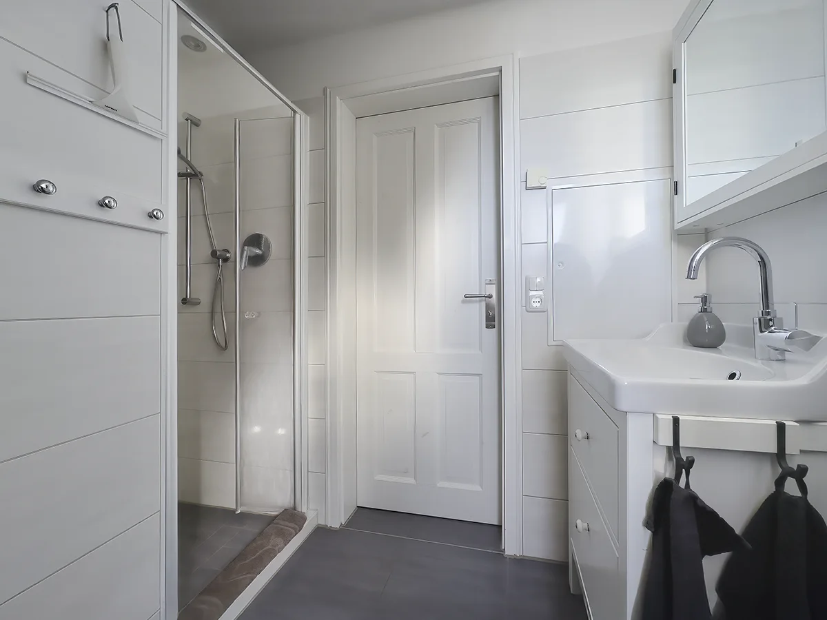 Modernes Tageslicht-Badezimmer der Wohnung 6 mit Dusche, weißem Waschtisch und hellen Fliesen.