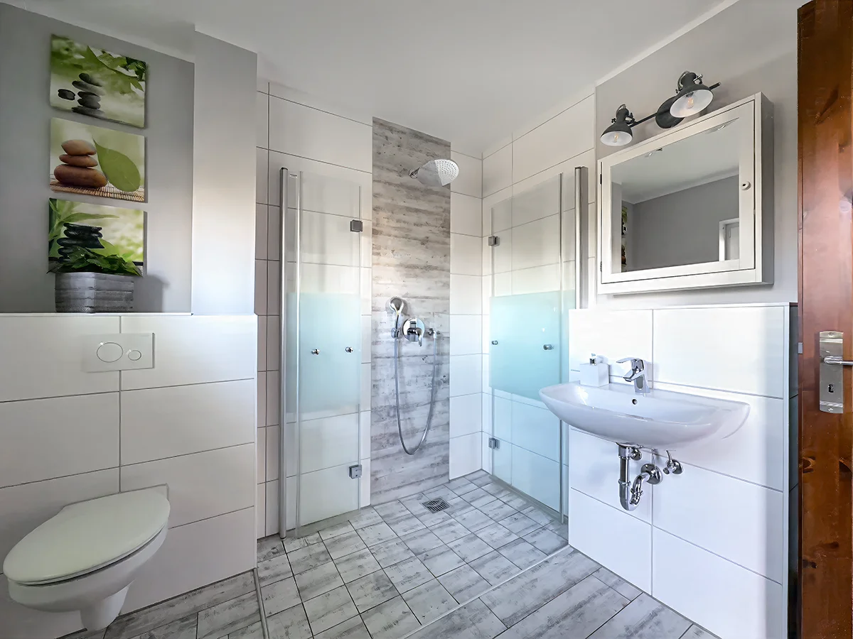Großzügiges Badezimmer der Ferienwohnung 8 mit bodengleicher Dusche, Holzoptik-Fliesen und großem Wandspiegel.