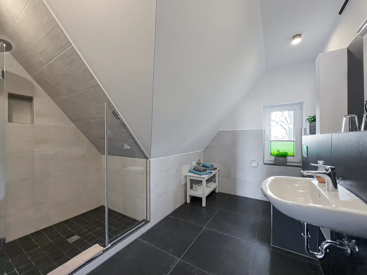 Modernes Tageslichtbad der Wohnung 10 mit verglaster Dusche, Badewanne und dunklen Bodenfliesen im Dachgeschoss.