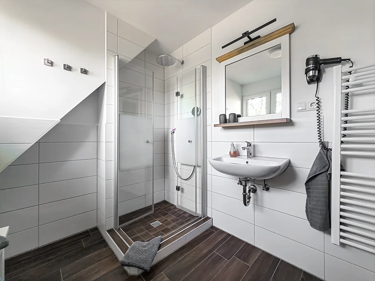 Modernes Badezimmer der Wohnung 9 mit verglaster Dusche, großem Waschbecken und hellen Fliesen in Steinoptik.