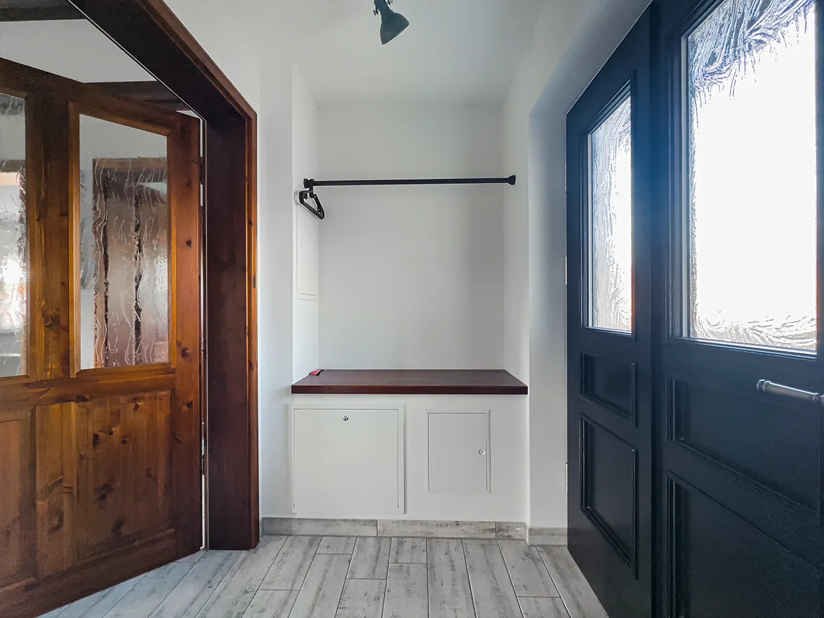Geräumiger Eingangsbereich der Wohnung 8 mit schwarzer Doppeltür, Holzstuhl und stilvoller Wandgarderobe.