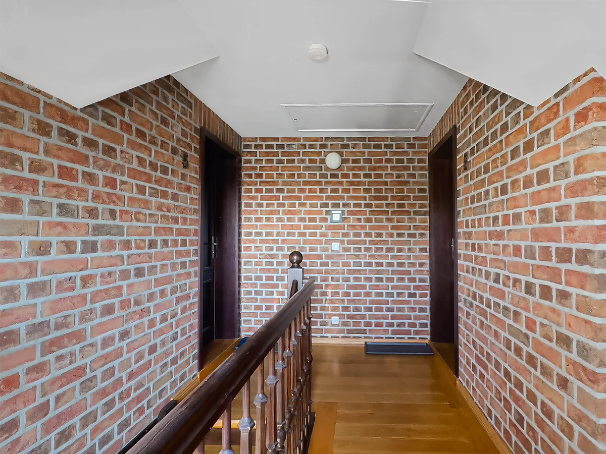 Eindrucksvoller Flurbereich im Obergeschoss mit rustikaler Sichtmauerwerk-Wand aus Backstein und Holzgeländer.