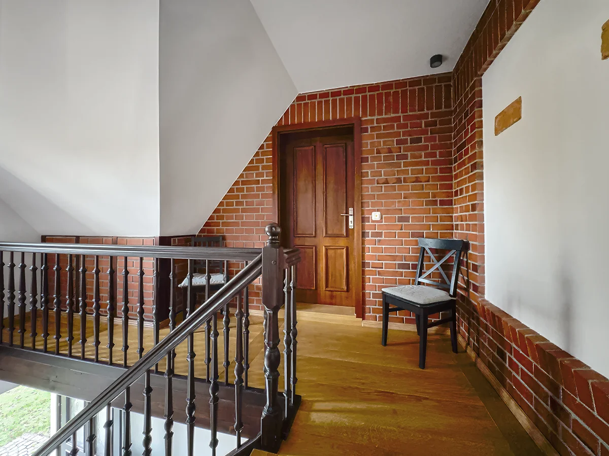 Oberer Flurbereich im Haus 2 mit historischer roter Backsteinwand, dunklem Holzgeländer und Treppenaufgang zur Wohnung 10