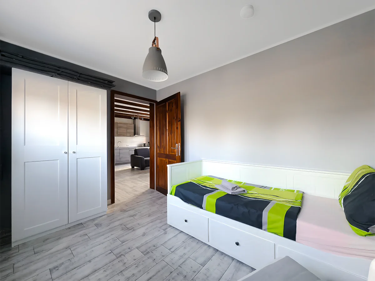 Schlafzimmer der Wohnung 8 mit massivem Holzbett, grüner Bettwäsche und zwei Fenstern für ein helles Ambiente