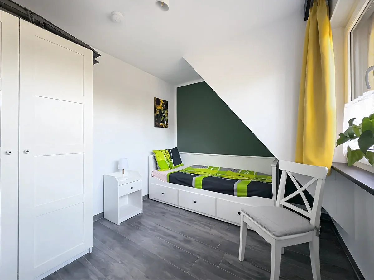 Zweites Schlafzimmer der Ferienwohnung 10 unter der Dachschräge mit Einzelbett, grünem Dekor und hellem Laminatboden.