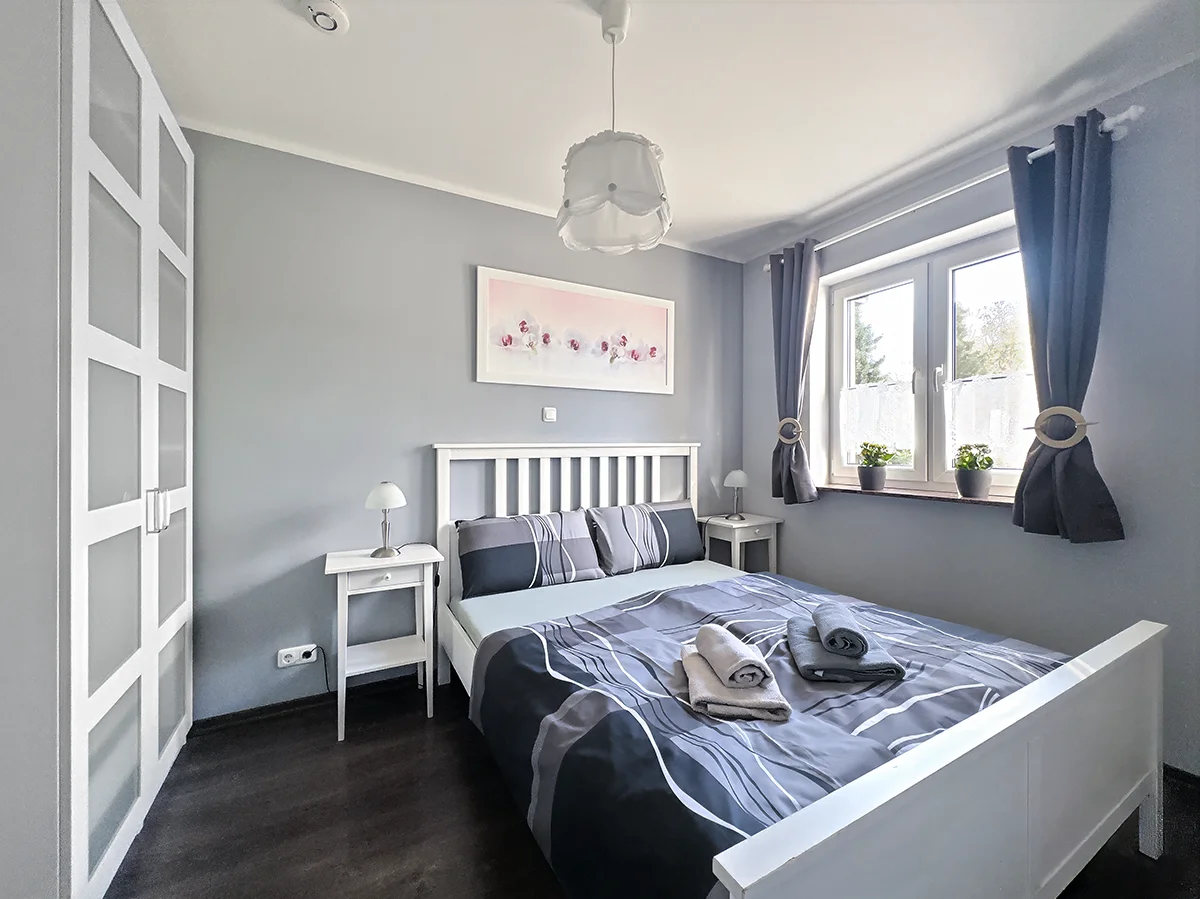 Modernes Schlafzimmer der Wohnung 2 mit weißem Doppelbett, Nachttischen und Blick aus dem Fenster in Markkleeberg