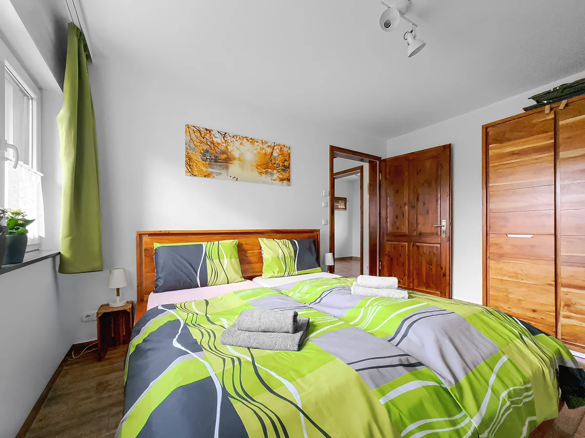 Schlafzimmer der Wohnung 7 mit Doppelbett, Bettwäsche und Blick aus dem Fenster.