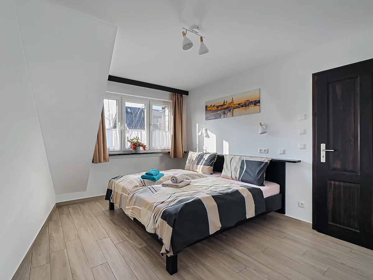 Helles Schlafzimmer der Wohnung 9 mit gemütlichem Bett, blau-grauer Bettwäsche und großem Kleiderschrank.