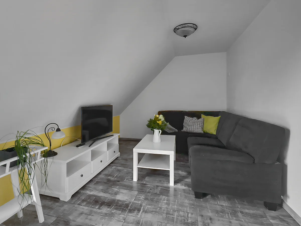 Wohnbereich der Ferienwohnung 6 mit grauem Ecksofa, weißem Sideboard und Flachbild-TV unter der Dachschräge