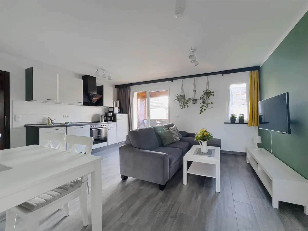 Helle Wohnküche der Ferienwohnung 10 in Markkleeberg mit modernen weißen Fronten, Kaffeestation und gemütlichem Sofa-Eck.