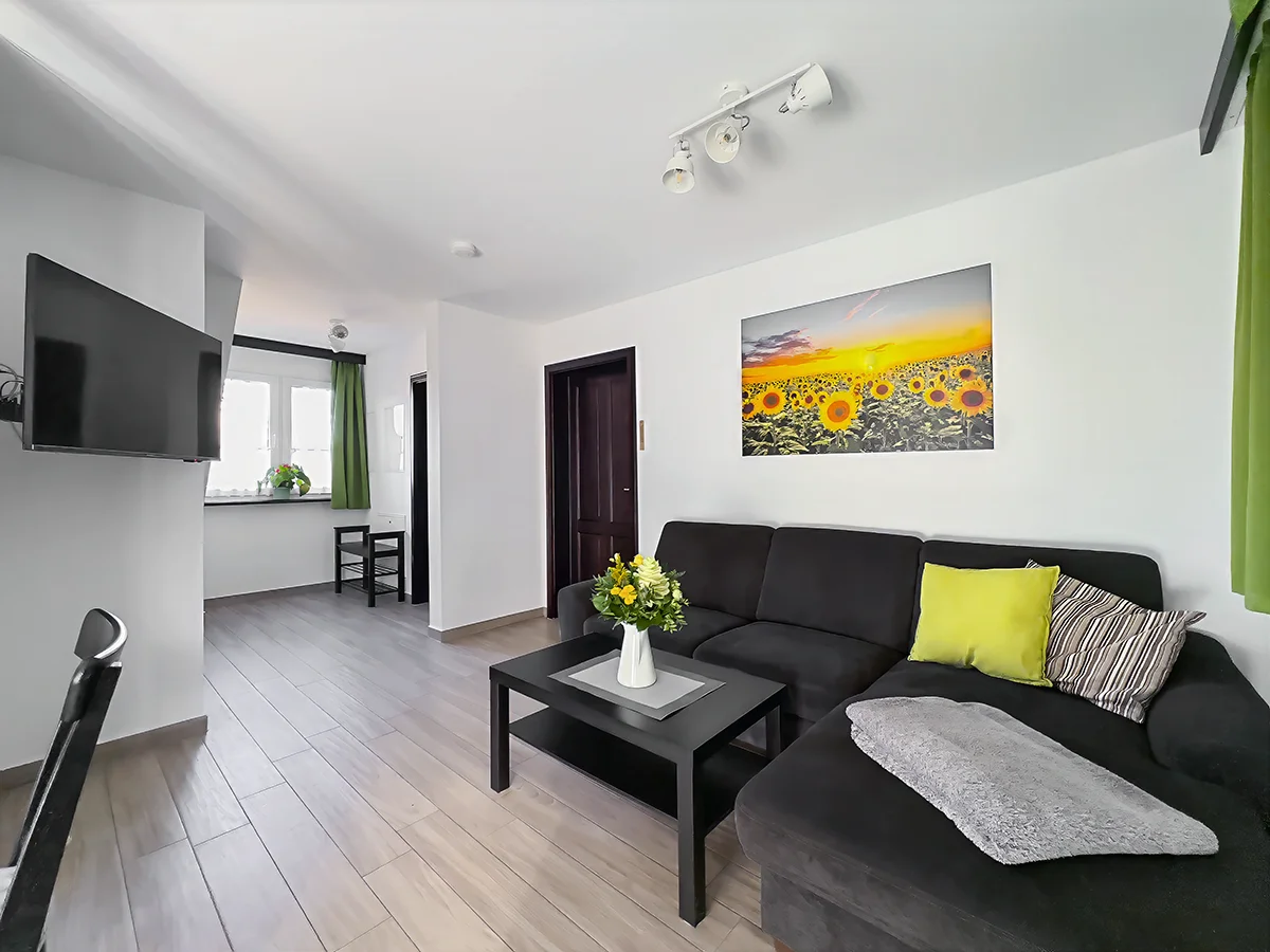 Modernes Wohnzimmer der Ferienwohnung 9 mit dunkelblauem Ecksofa, hellem Laminatboden und dekorativen Holzbalken an der Decke.